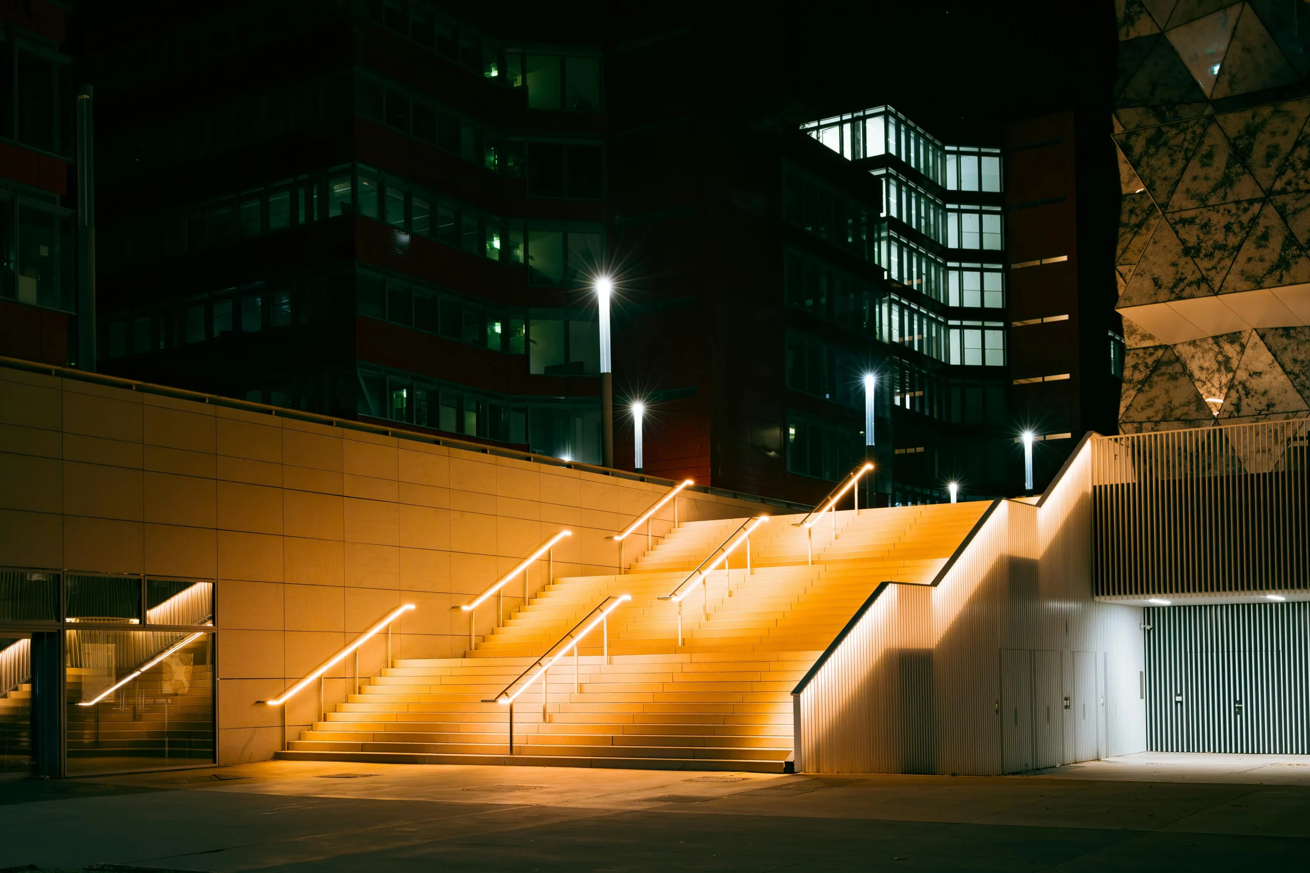 Escalier extérieur illuminé de nuit dans le quartier du Kirchberg à Luxembourg, entouré de bâtiments modernes.